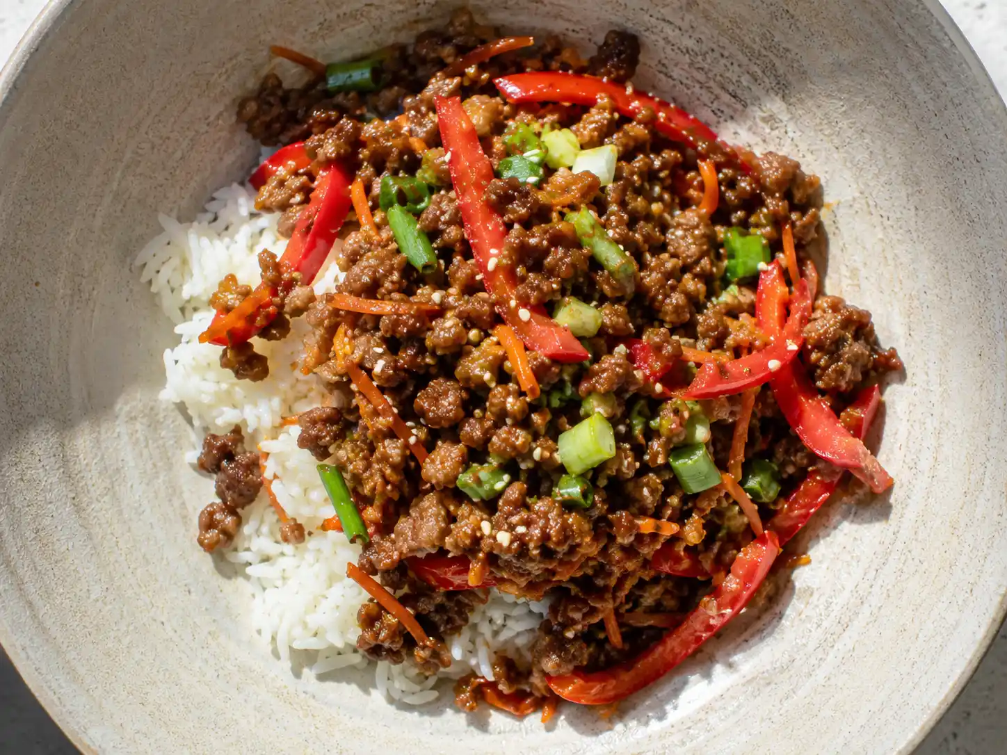 asiatisk köttfärs i skål med ris, paprika, morot, salladslök och sesam i blank sojasås