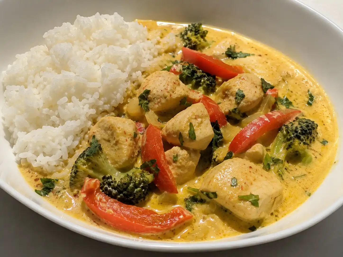 asiatisk kycklinggryta i skål med krämig kokosås, kycklingbitar, paprika, broccoli och ris bredvid