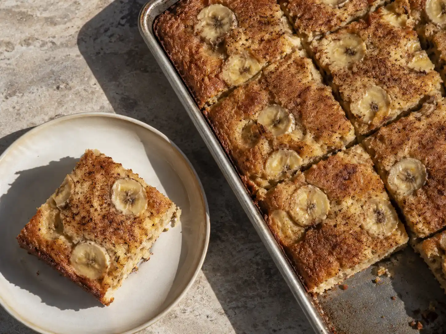 banankaka långpanna skuren i mjuka rutor med gyllene yta, bakade bananskivor och lite kanel