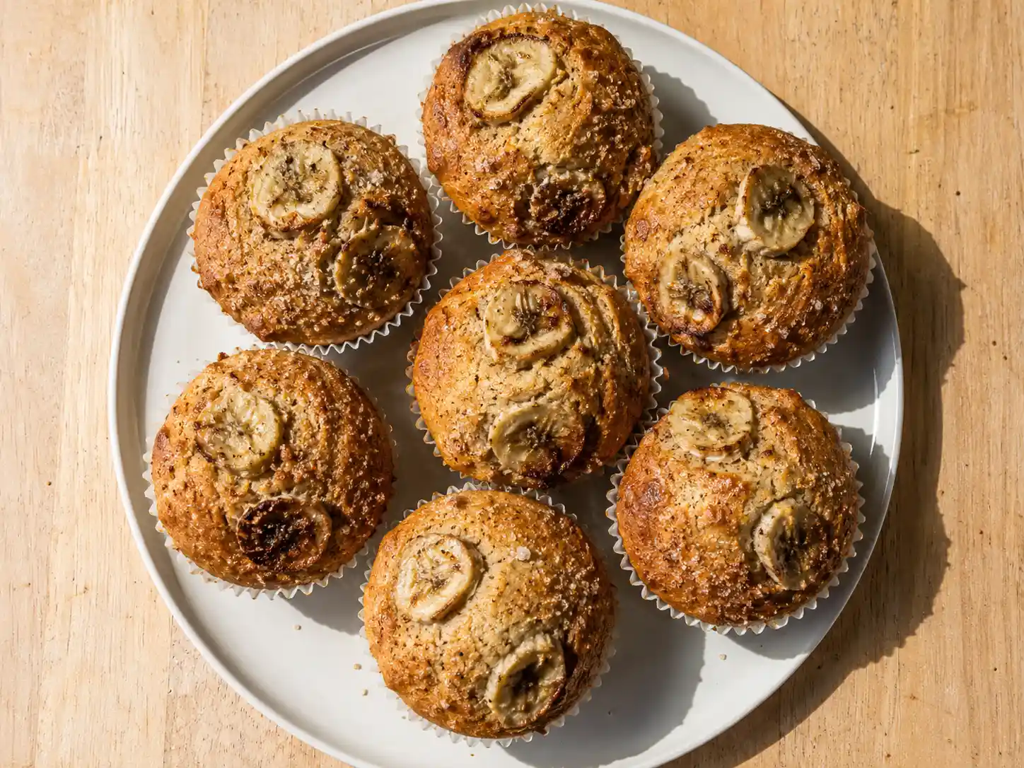 bananmuffins med gyllene toppar, bananskivor och mjuk smula i pappersformar på ett fat