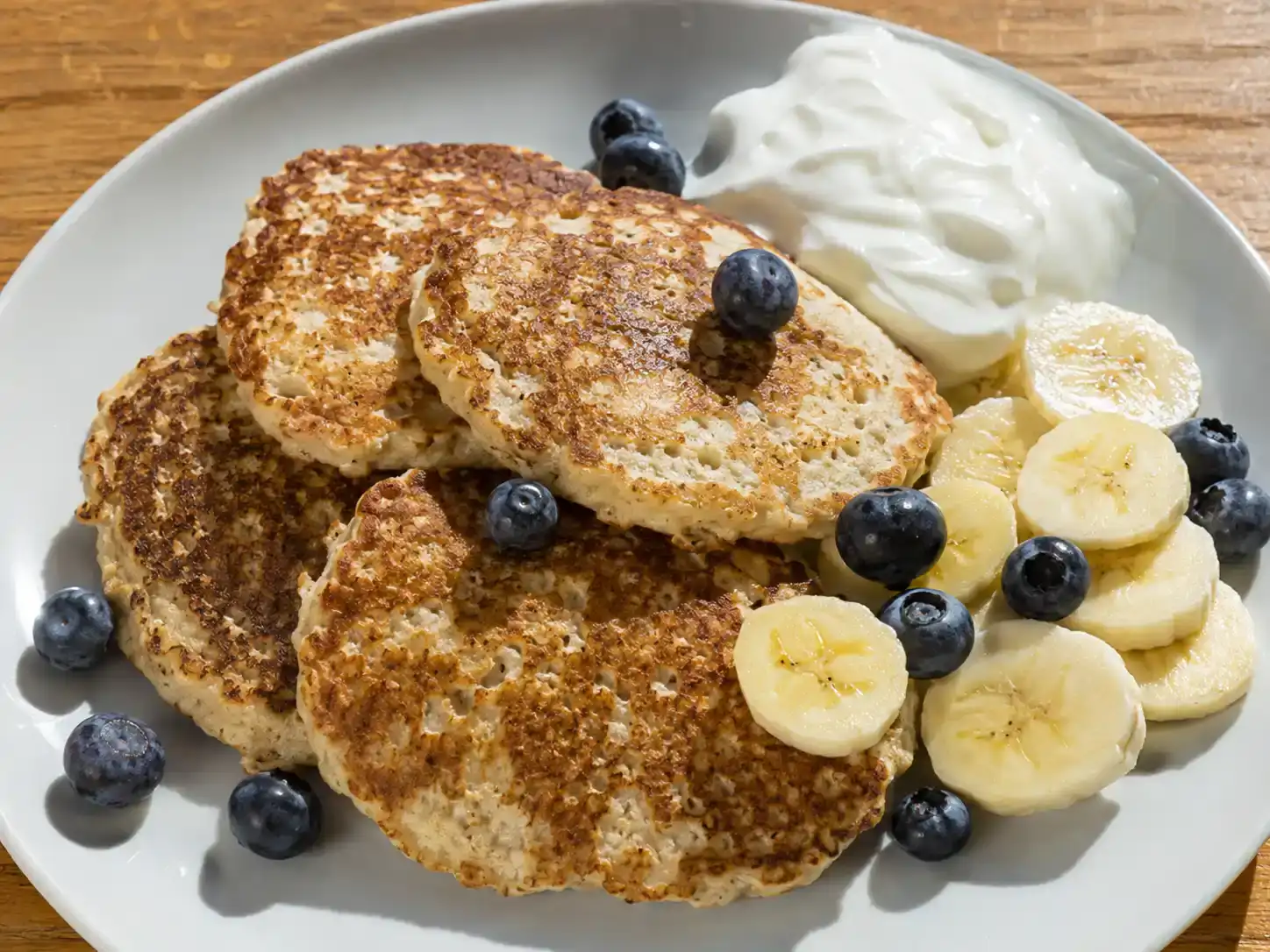 bananpannkakor med gyllenbrun yta, skivad banan, blåbär och yoghurt på en ljus tallrik