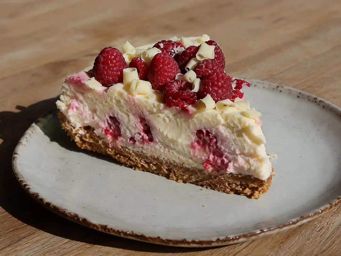 cheesecake hallon vit choklad på tallrik med kexbotten, vit fyllning och blank hallontopp