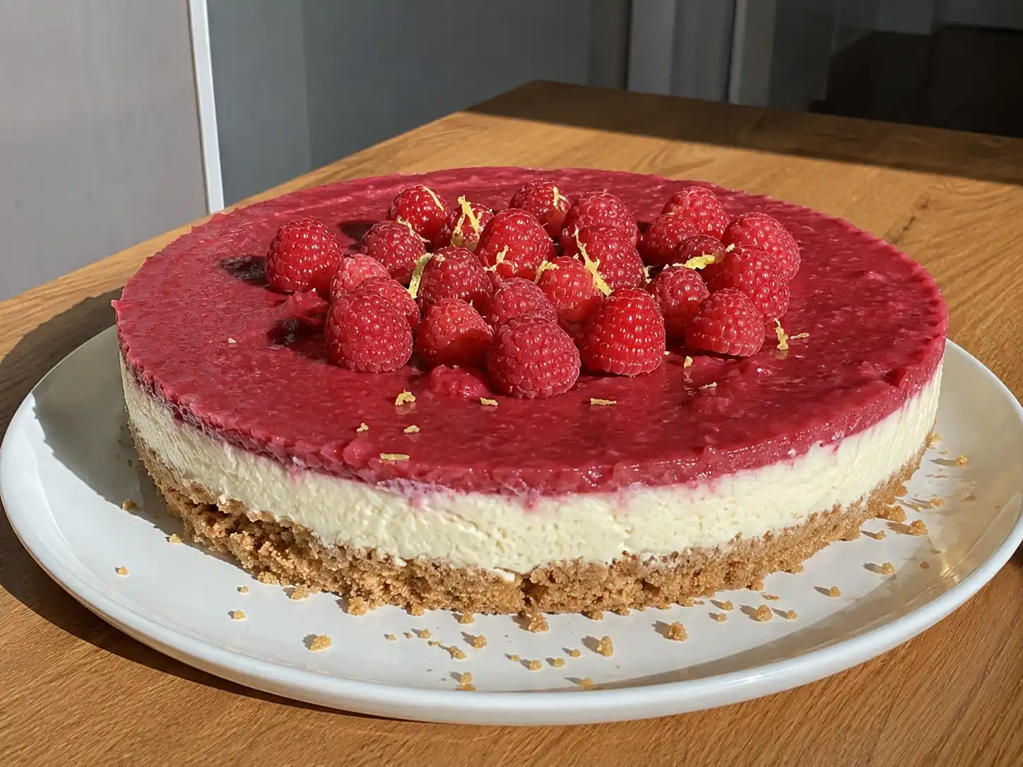 Cheesecake med hallon med smulig kexbotten, len färskostfyllning och blank hallontopp på ett vitt fat