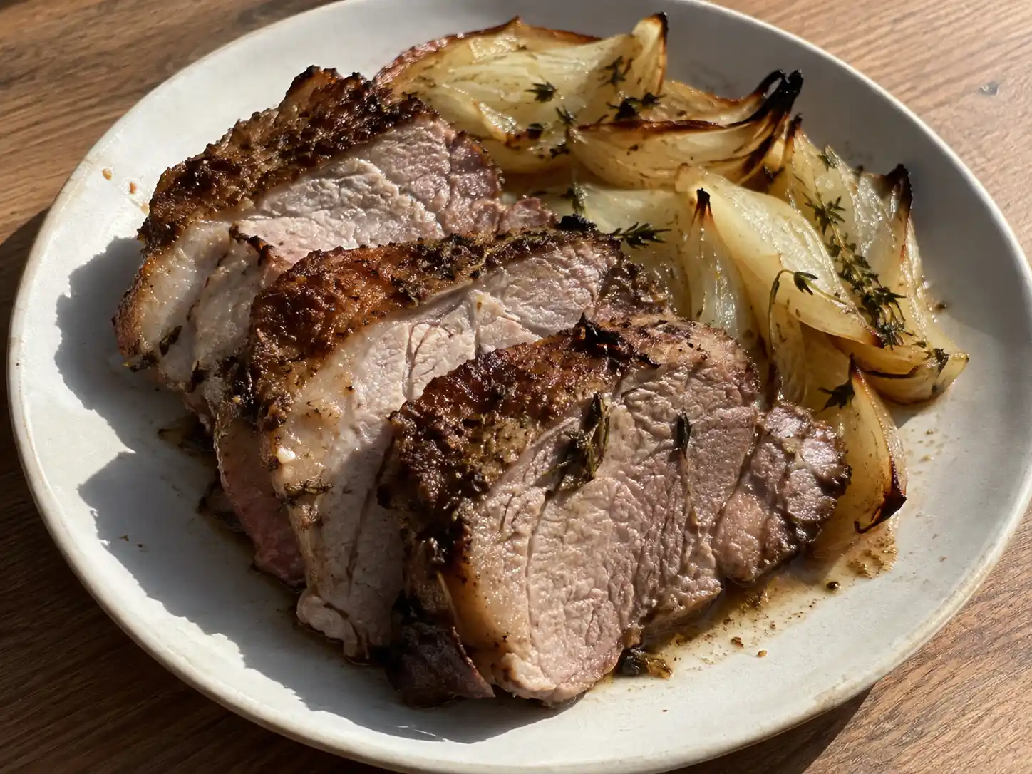 fläskkarre i ugn skivad på tallrik med brynt yta, saftigt kött, rostad lök och sky från formen