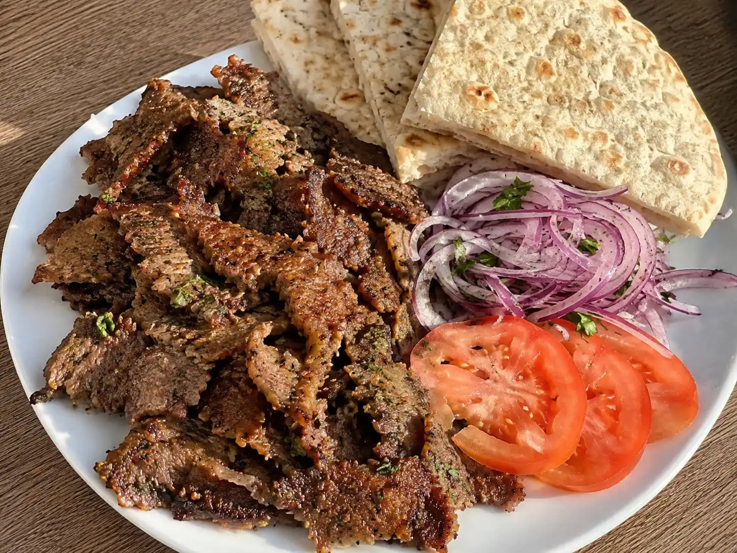 hemmagjord kebab köttfärs i tunna brynta skivor med tomat, rödlök, persilja och pitabröd på tallrik