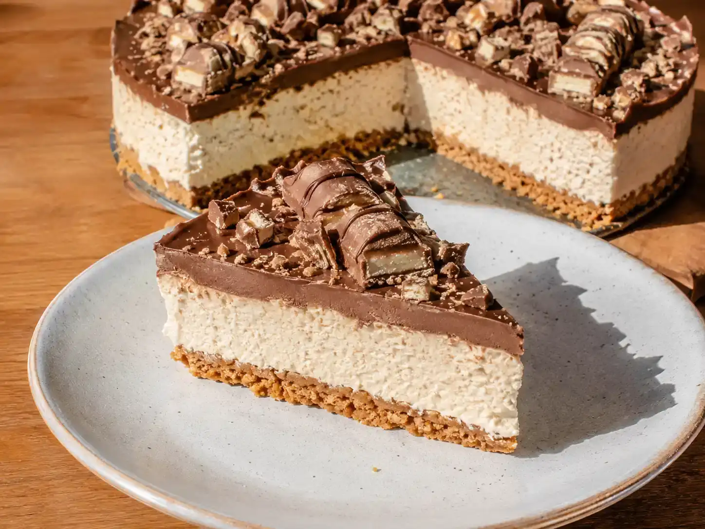 kinder cheesecake på tallrik med krämig fyllning, kexbotten, blank chokladtopp och bitar av Kinder