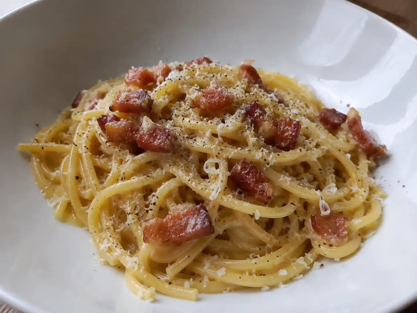 klassisk carbonara serverad nykokt med spaghetti, gyllene pancetta, riven pecorino och svartpeppar i djup tallrik hemma.