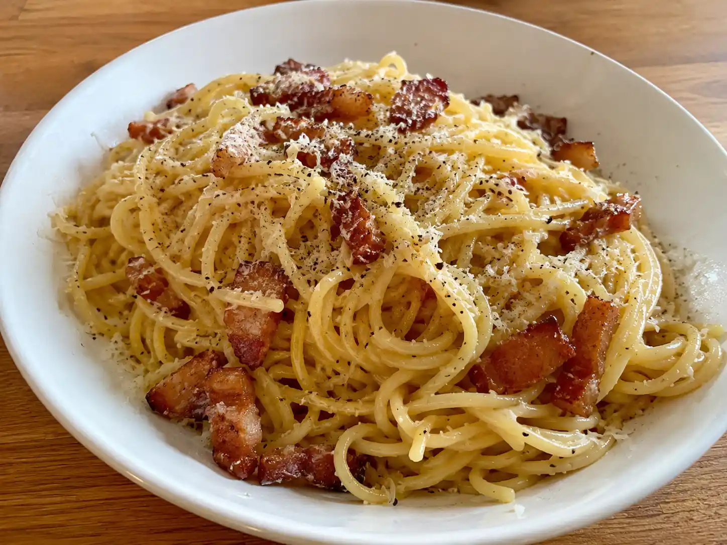 krämig carbonara serverad direkt ur skål med spaghetti, pancetta, riven parmesan och svartpeppar i blank, len sås.