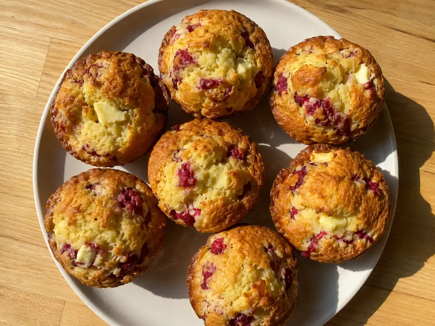 muffins med hallon och vit choklad på tallrik med gyllene toppar, röda bär och smält choklad