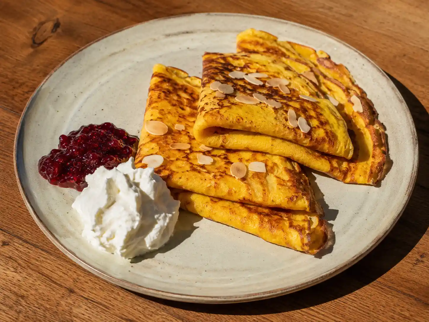 pannkakor med saffran på tallrik med gyllengul yta, lingon, grädde och lätt frasiga kanter