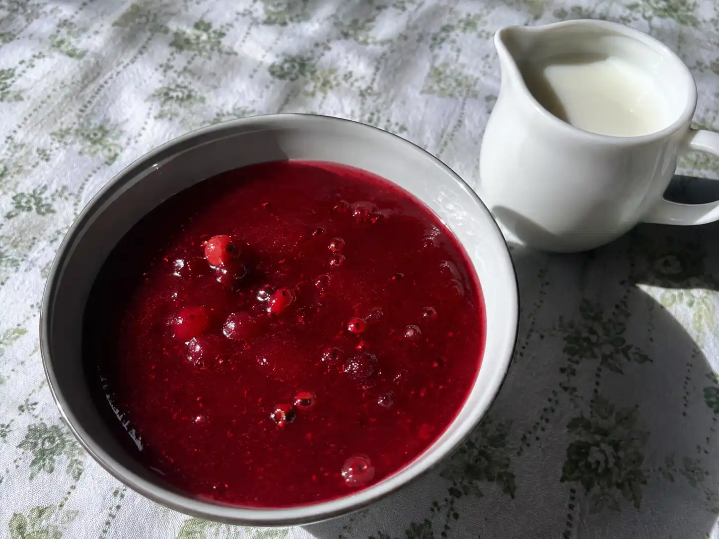 röda vinbär kräm i skål med blank röd yta, hela bär och mjölk vid sidan för enkel servering