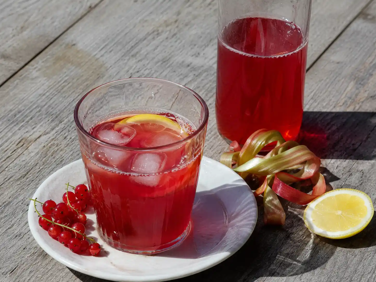 röda vinbär och rabarbersaft i glas och flaska med klar rubinröd färg, is och bär vid sidan