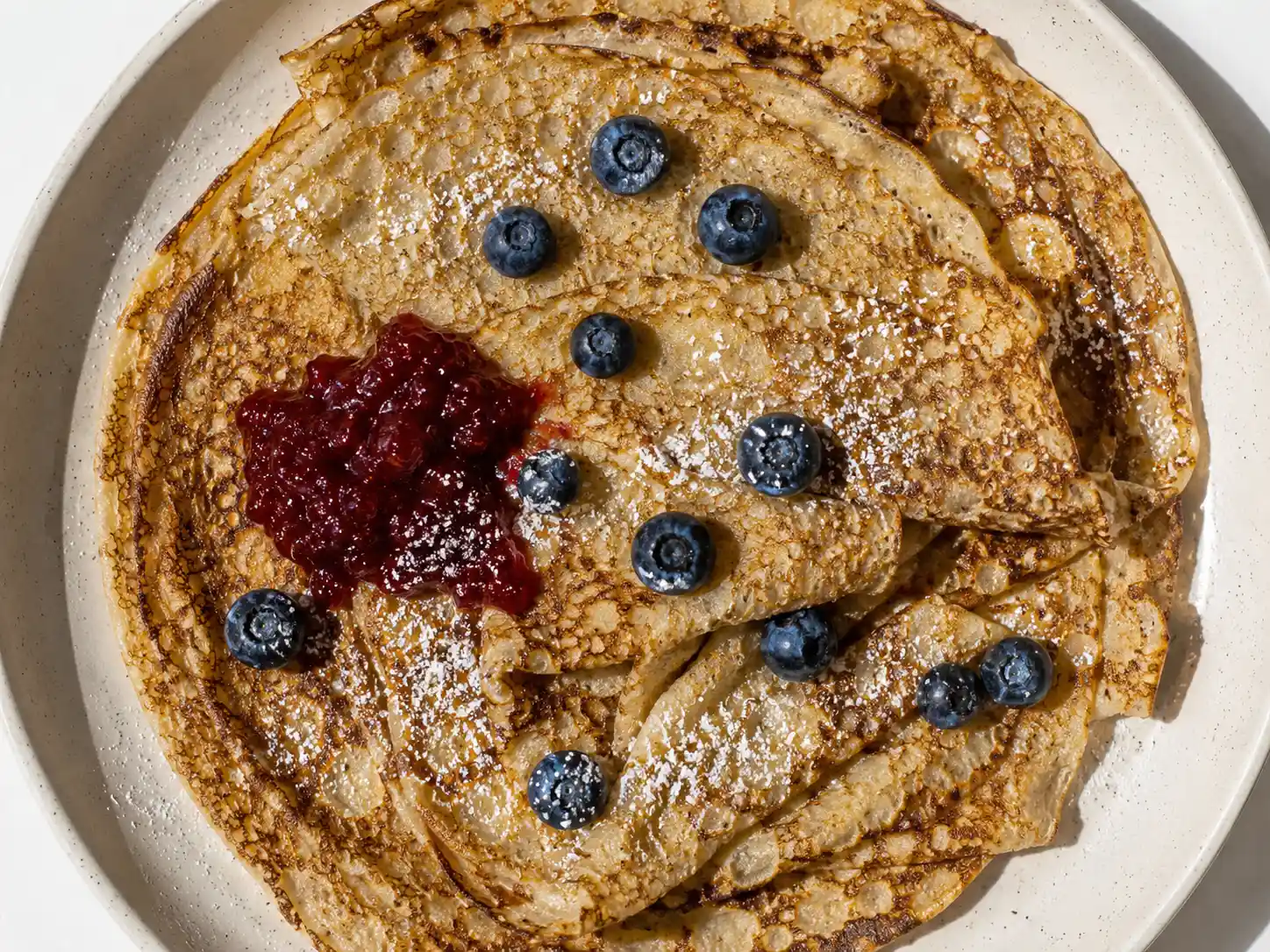 veganska pannkakor staplade på tallrik med sylt, bär och tydligt gyllene stekyta