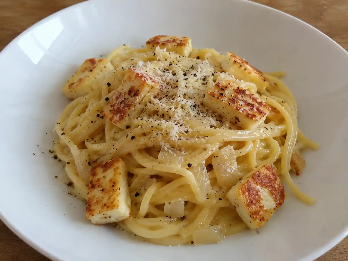 vegetarisk carbonara serverad nykokt med spaghetti, gyllene halloumi, svartpeppar och krämig sås i djup tallrik.