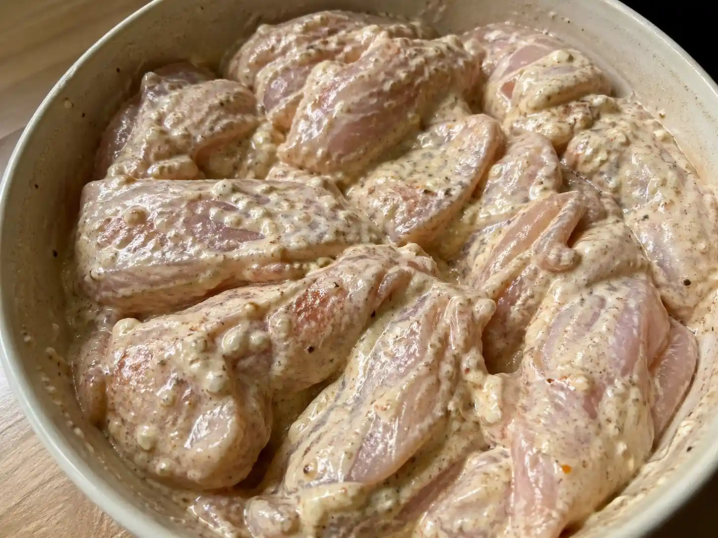 Rå kyckling täckt med yoghurtmarinad, vitlök, paprika och svartpeppar i en enkel skål.