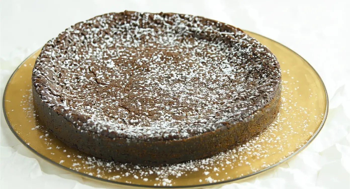 En tårtbit kladdkaka med mörk choklad som visar en perfekt seg mitt, serverad med grädde på en assiett.