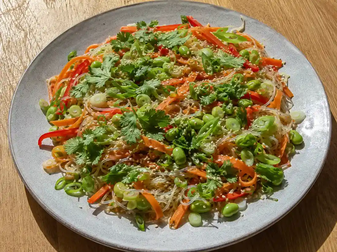 asiatisk glasnudelsallad med gurka, morot, paprika, edamame, sesam och färska örter på ett fat