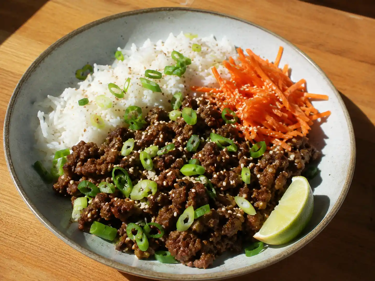 asiatisk köttfärs med ris med brynt färs, morot, salladslök, sesamfrön och lime på ljus tallrik