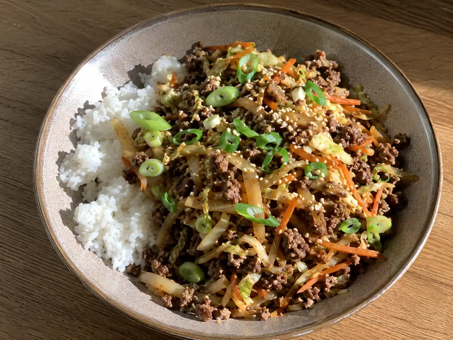 asiatisk köttfärs med vitkål i stekpanna med ris, salladslök, lime och rostad sesam på bordet