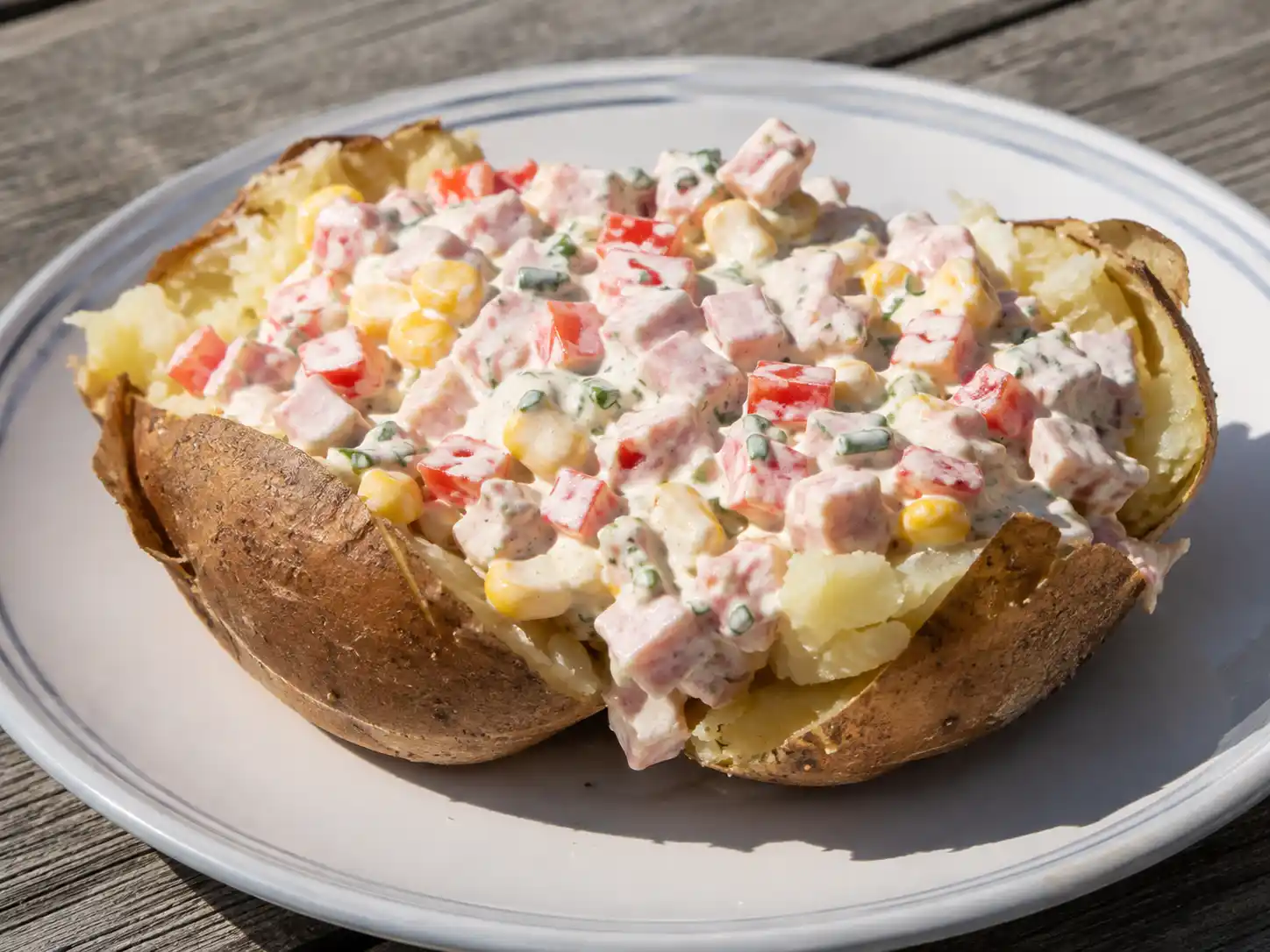 bakad potatis skinkröra med fluffig potatis, rökt skinka, röd paprika, majs och gräslök på tallrik
