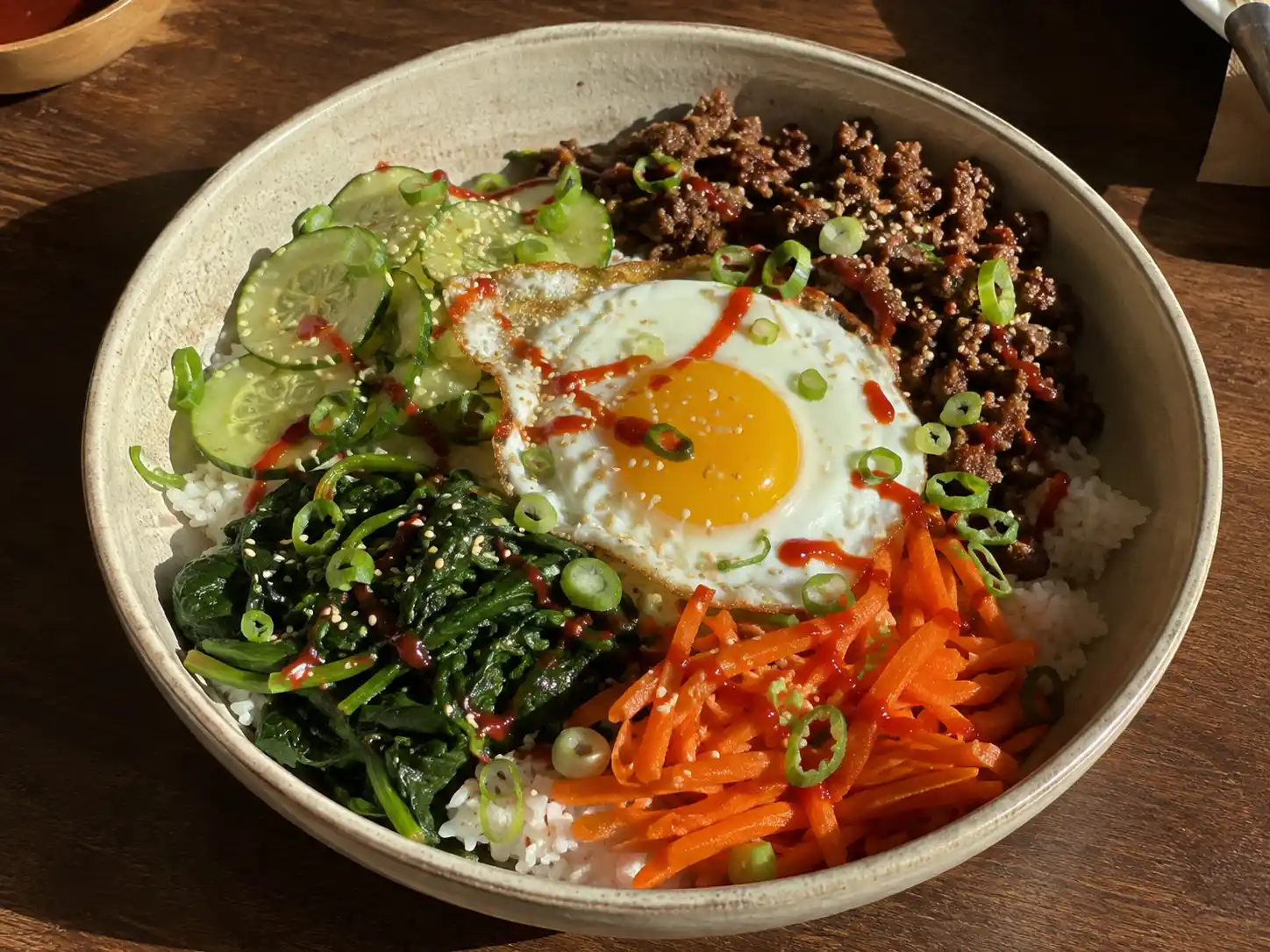 bibimbap köttfärs i skål med ris, morot, spenat, gurka, stekt ägg, sesam och gochujangsås