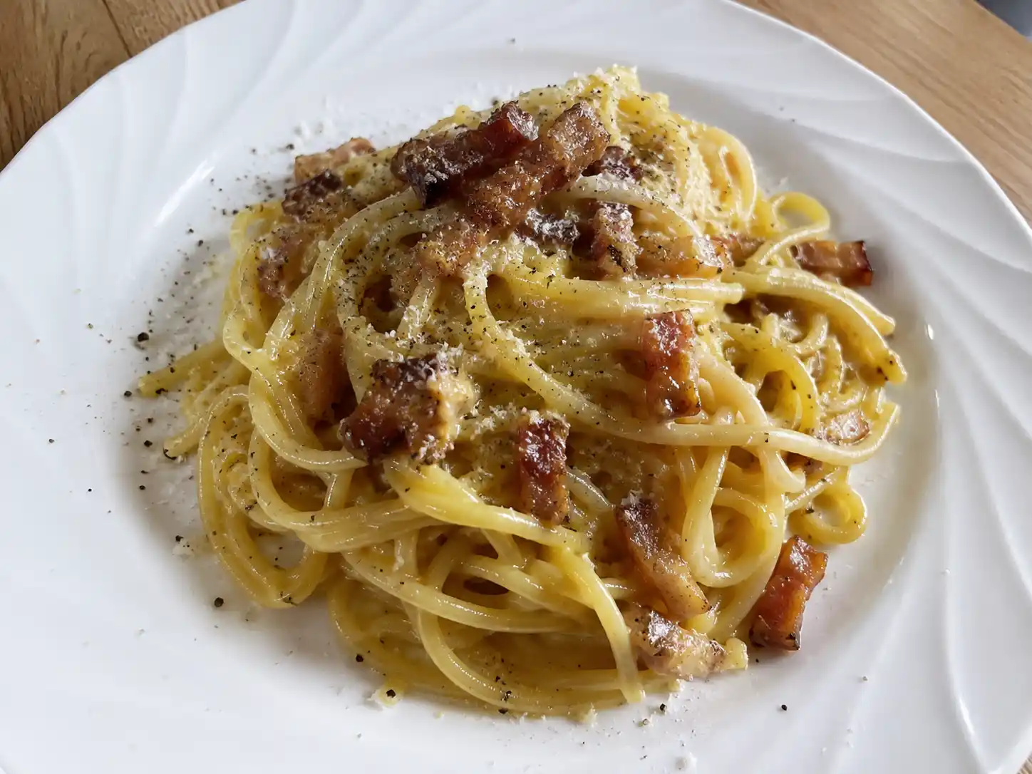 enkel pasta carbonara på tallrik med spaghetti, pancetta, pecorino och svartpeppar i krämig sås hemma i naturligt ljus.