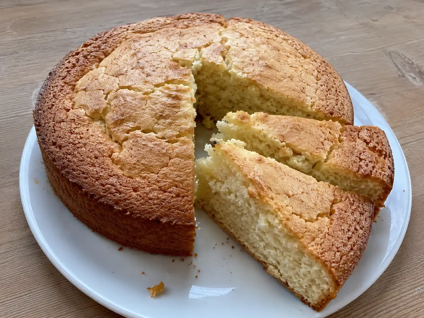 enkel sockerkaka på fat, gyllene och lätt sprucken på toppen, skuren i bitar på ett enkelt köksbord