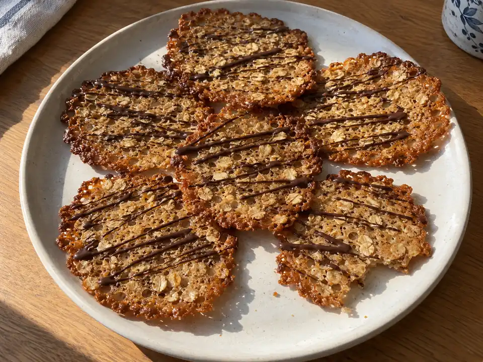 havreflarn med tunna gyllene kanter, synliga havregryn och smala mörka chokladstråk på ett enkelt fat.