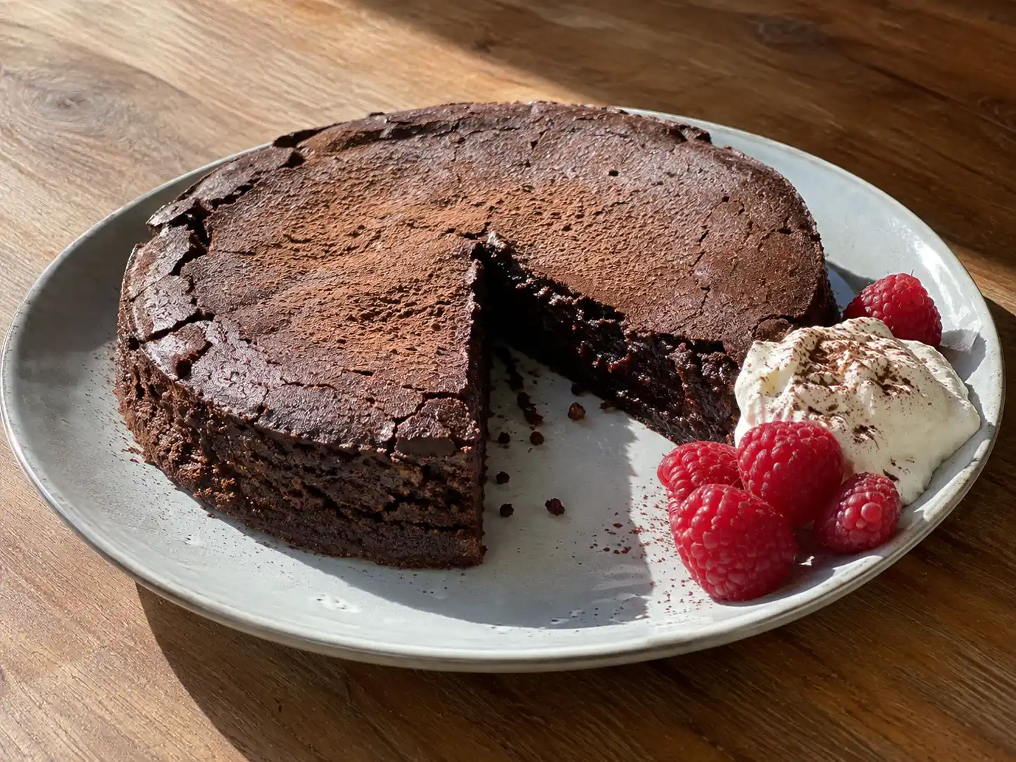 Kladdkaka utan ägg med seg kant och kladdig chokladmitt, serverad med lättvispad grädde och hallon.