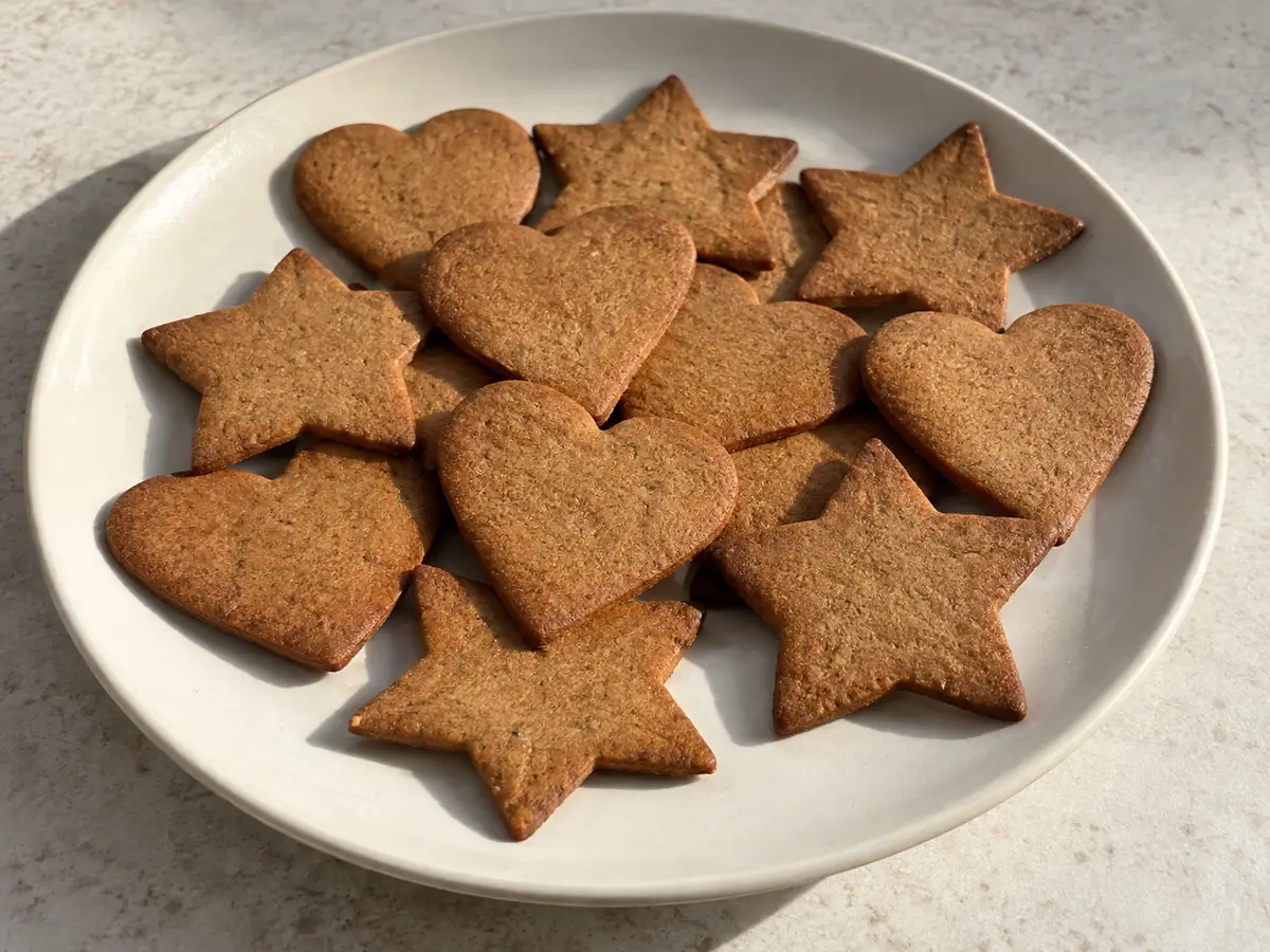 Tunna bruna pepparkakor formade som hjärtan och stjärnor, utan glasyr på ett enkelt keramikfat.