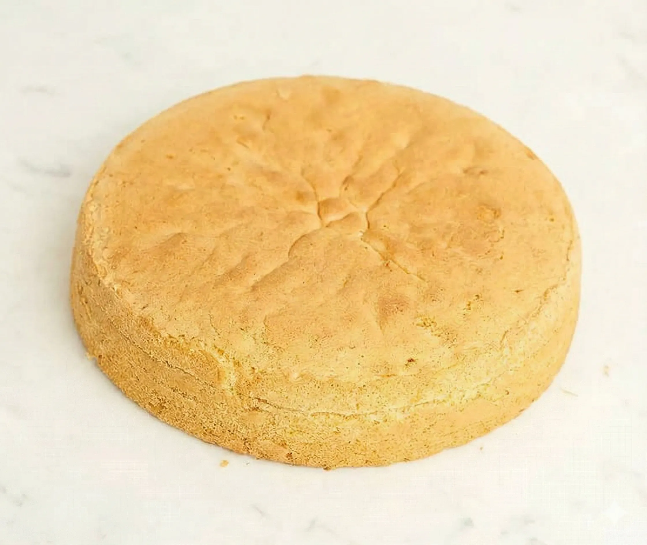 En nygräddad hög och luftig tårtbotten på ett galler redo att delas och fyllas med grädde.