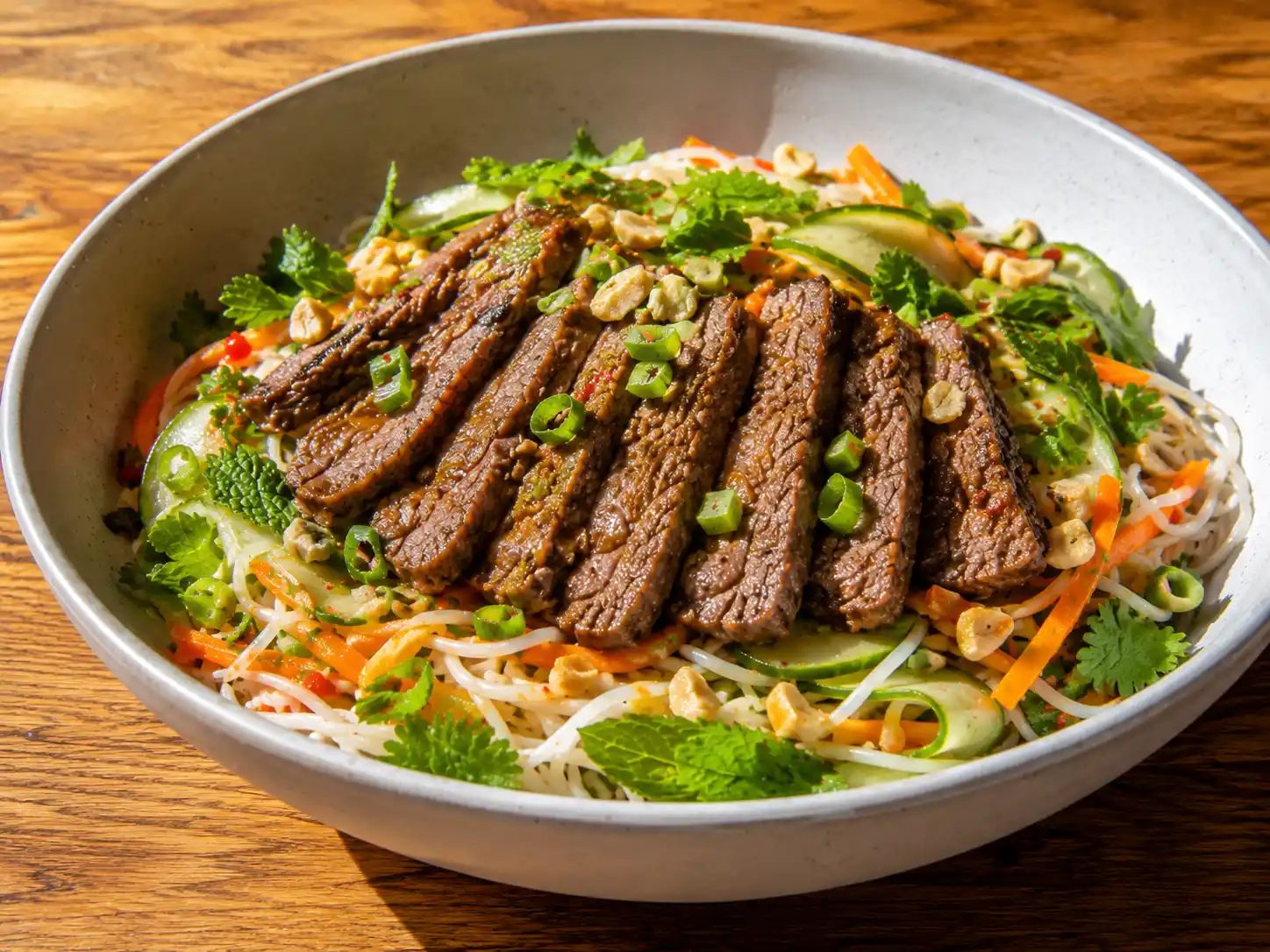 asiatisk biffsallad med skivad biff, risnudlar, gurka, koriander och jordnötter i skål