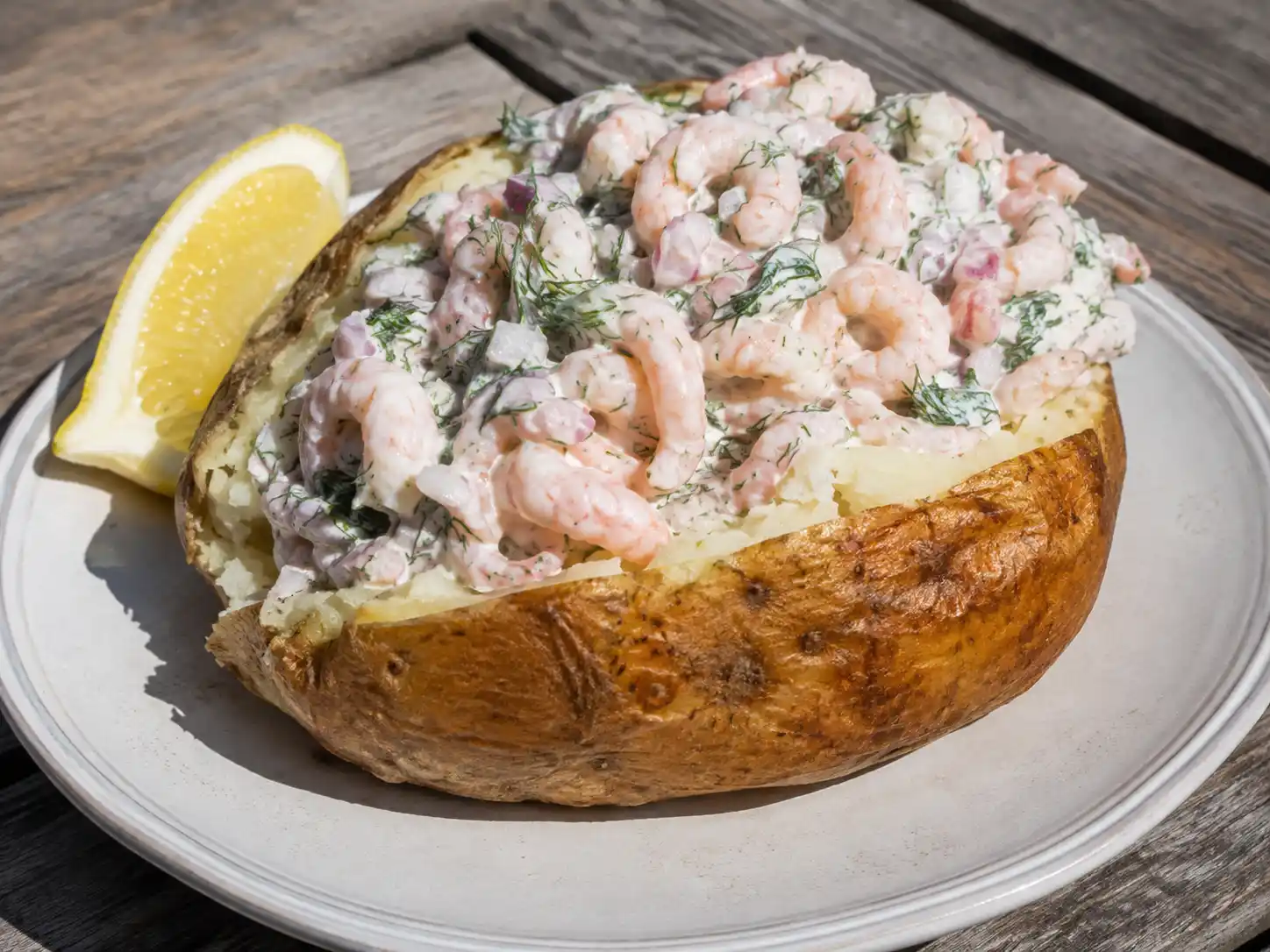 Bakad potatis med skagenröra med fluffig insida, krämiga räkor, dill, rödlök och citron på tallrik