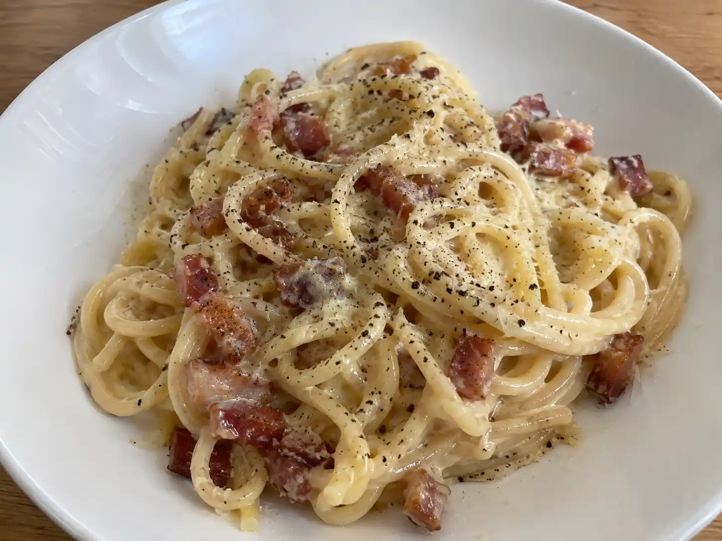 carbonara med grädde serverad i djup tallrik med spaghetti, bacon, riven parmesan och svartpeppar i krämig sås