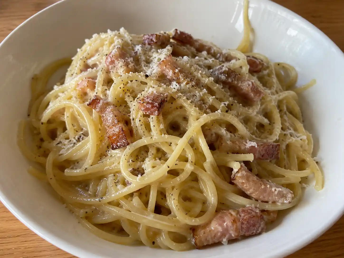 carbonara utan grädde i djup tallrik med blank sås, pecorino, svartpeppar och gyllene bitar av guanciale
