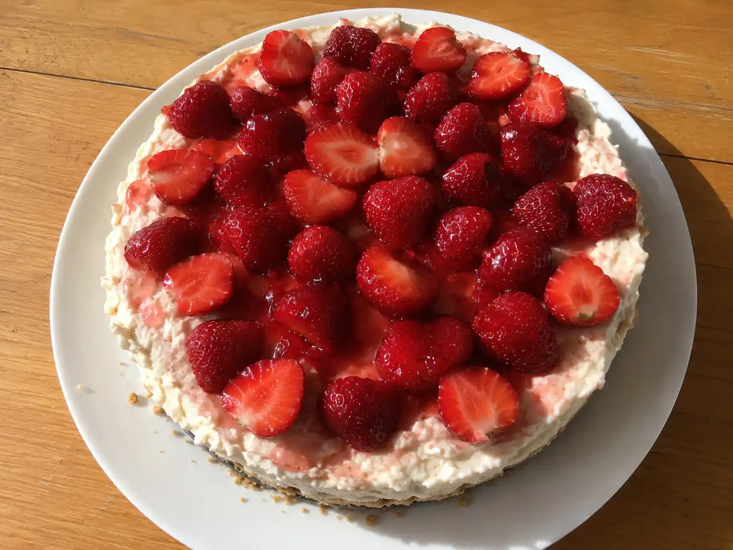 Cheesecake med jordgubbar ovanifrån, skuren i bitar med röda färska bär och krämig vit fyllning på spröd digestivebotten.