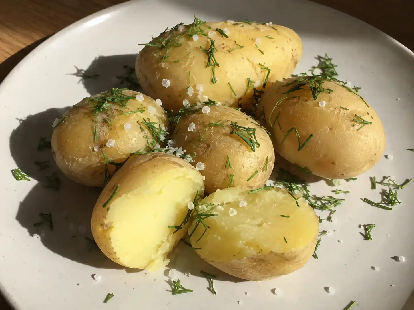 kokt potatis med torr fin yta, hackad dill och synliga saltkorn på en enkel tallrik