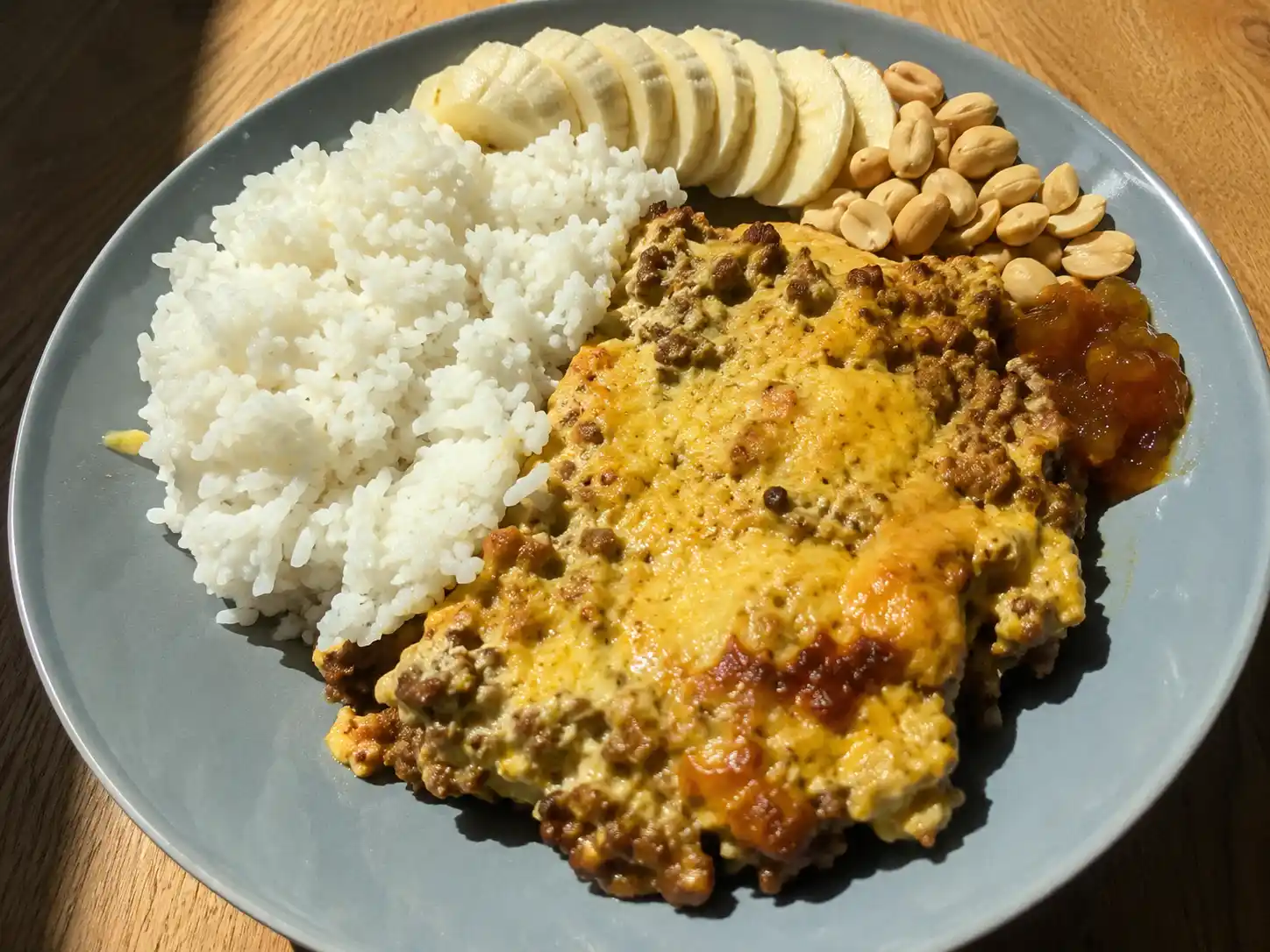 köttfärs africana med gyllene currytäcke, ris, skivad banan och rostade jordnötter på tallrik