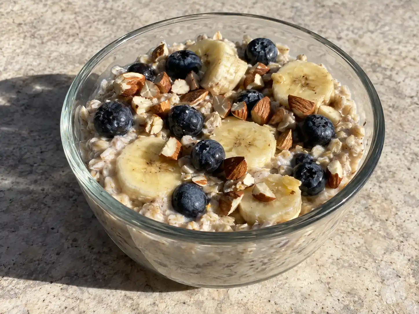 overnight oats i glas med krämig havregröt, bananskivor, blåbär och hackade nötter på toppen