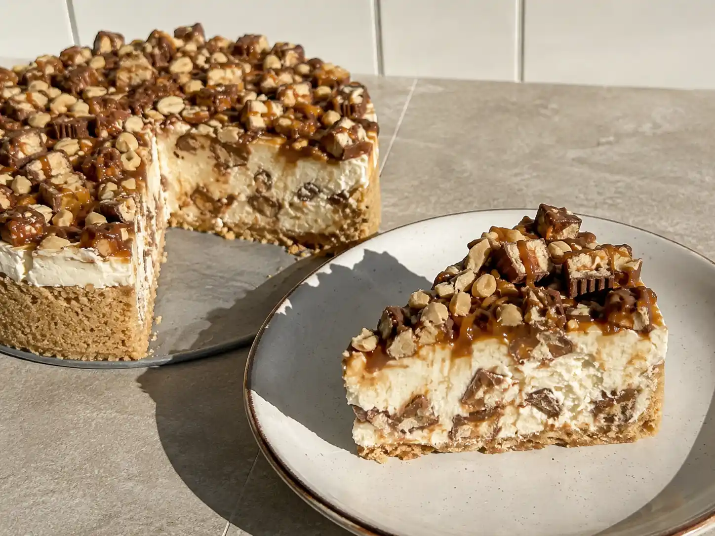 snickers cheesecake med kola, jordnötter och choklad på en enkel tallrik i dagsljus