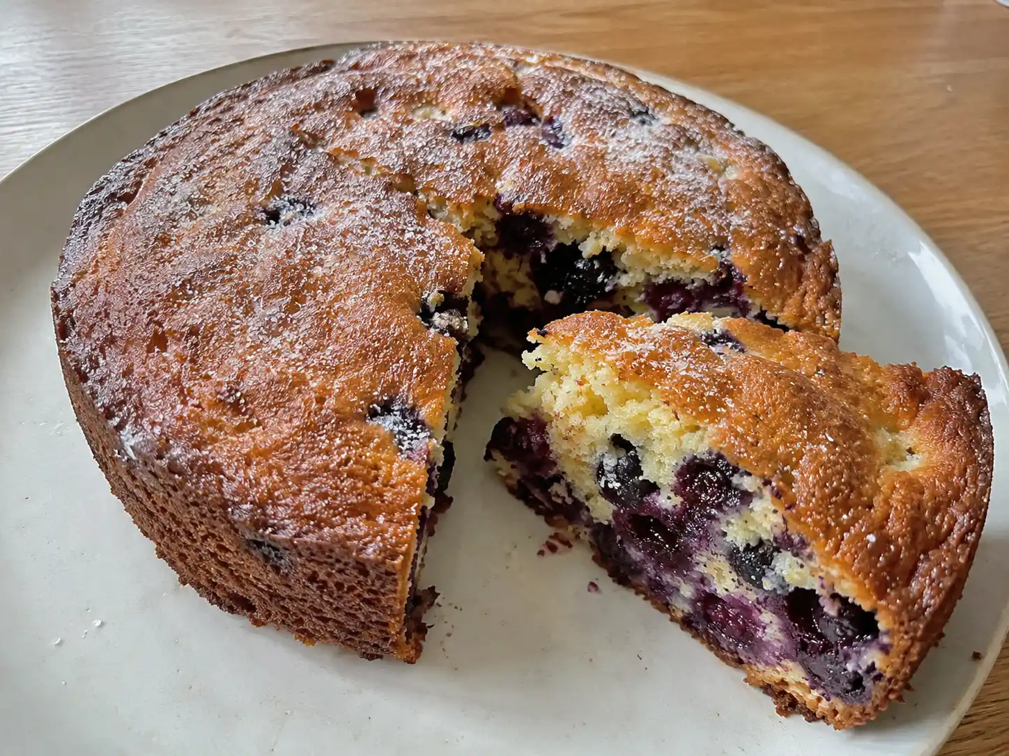 sockerkaka med blåbär på fat, skuren i skivor med saftig smula, gyllene yta och blåbär som syns i varje bit